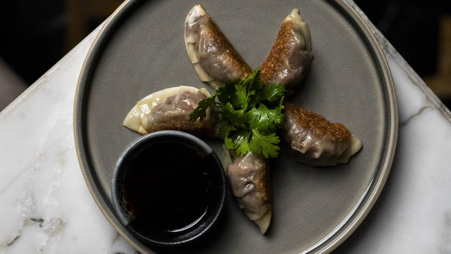 Wagyu gyoza with spicy ponzu served on a grey plate set atop a white marble table