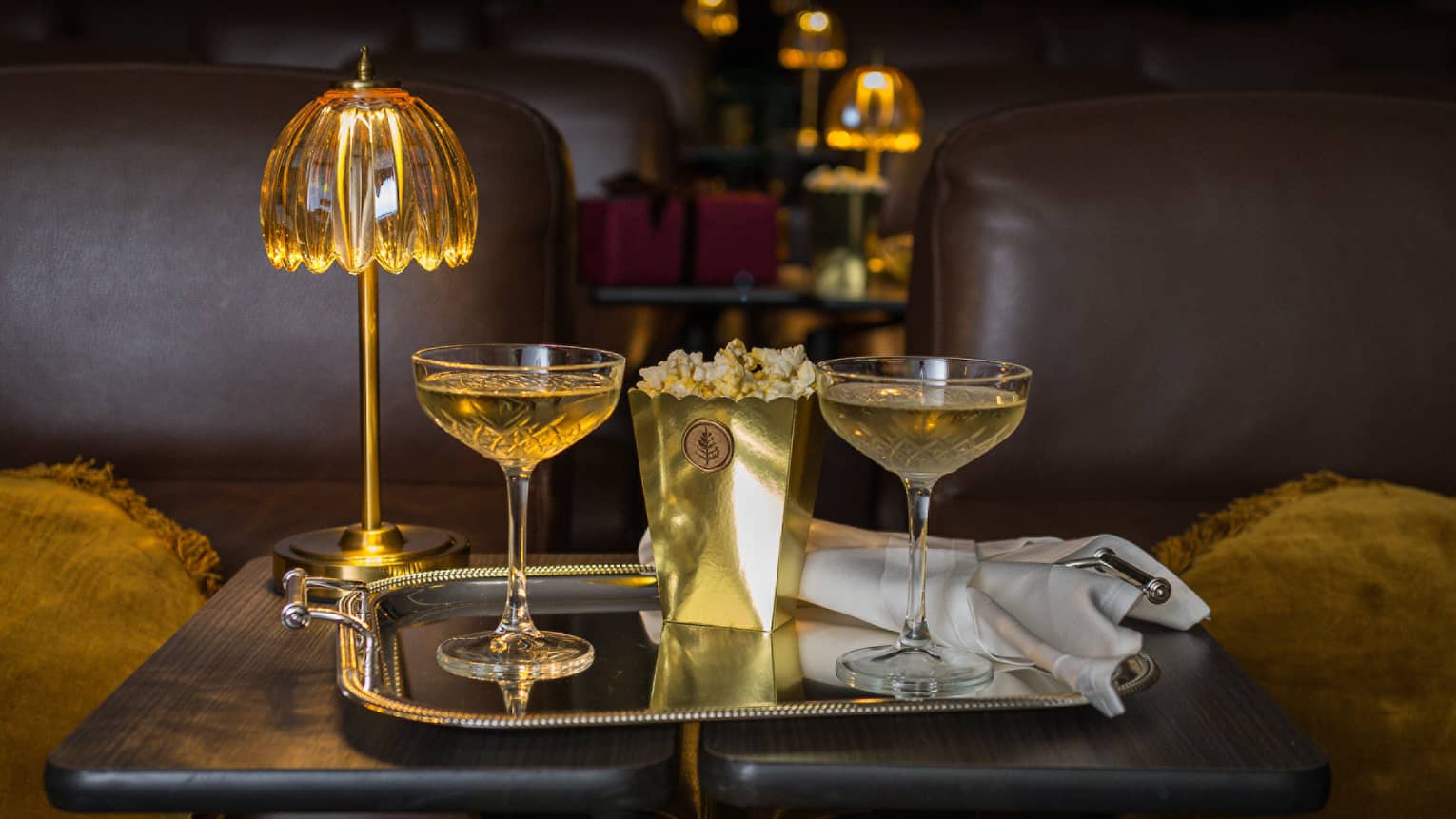 Two filled coupe glasses on a silver serving tray with popcorn in front of a golden dome light.