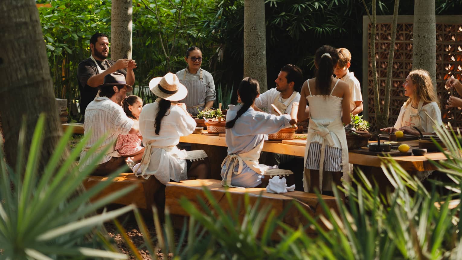 People seated around a long outdoor dining table set among palm trees