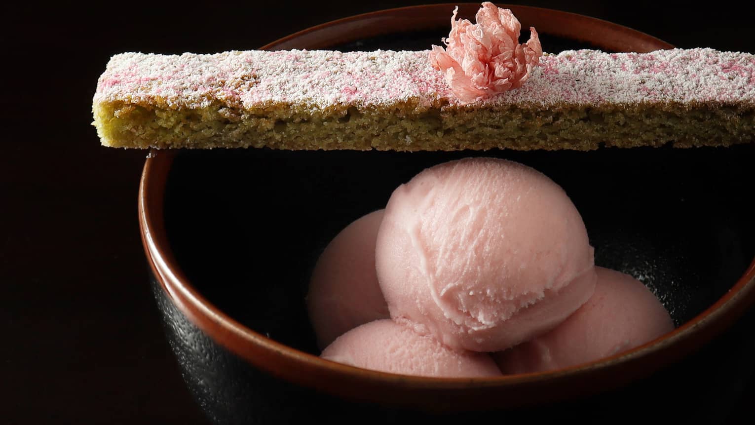 Light pink ice cream in a black bowl.