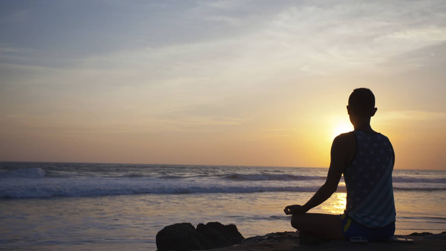 Silhouette of person sitting cross-legged, meditating in front of beach at sunset