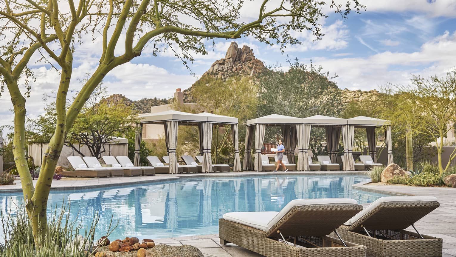 Outdoor pool with lounge chairs, canvas cabanas, staff member, rocky surroundings