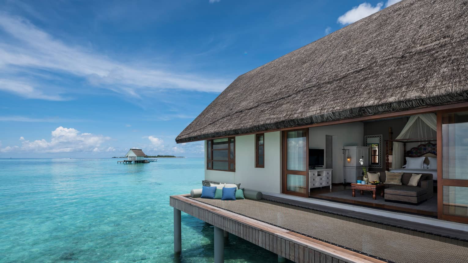 Overwater bungalow with thatched roof, set atop clear turquoise water