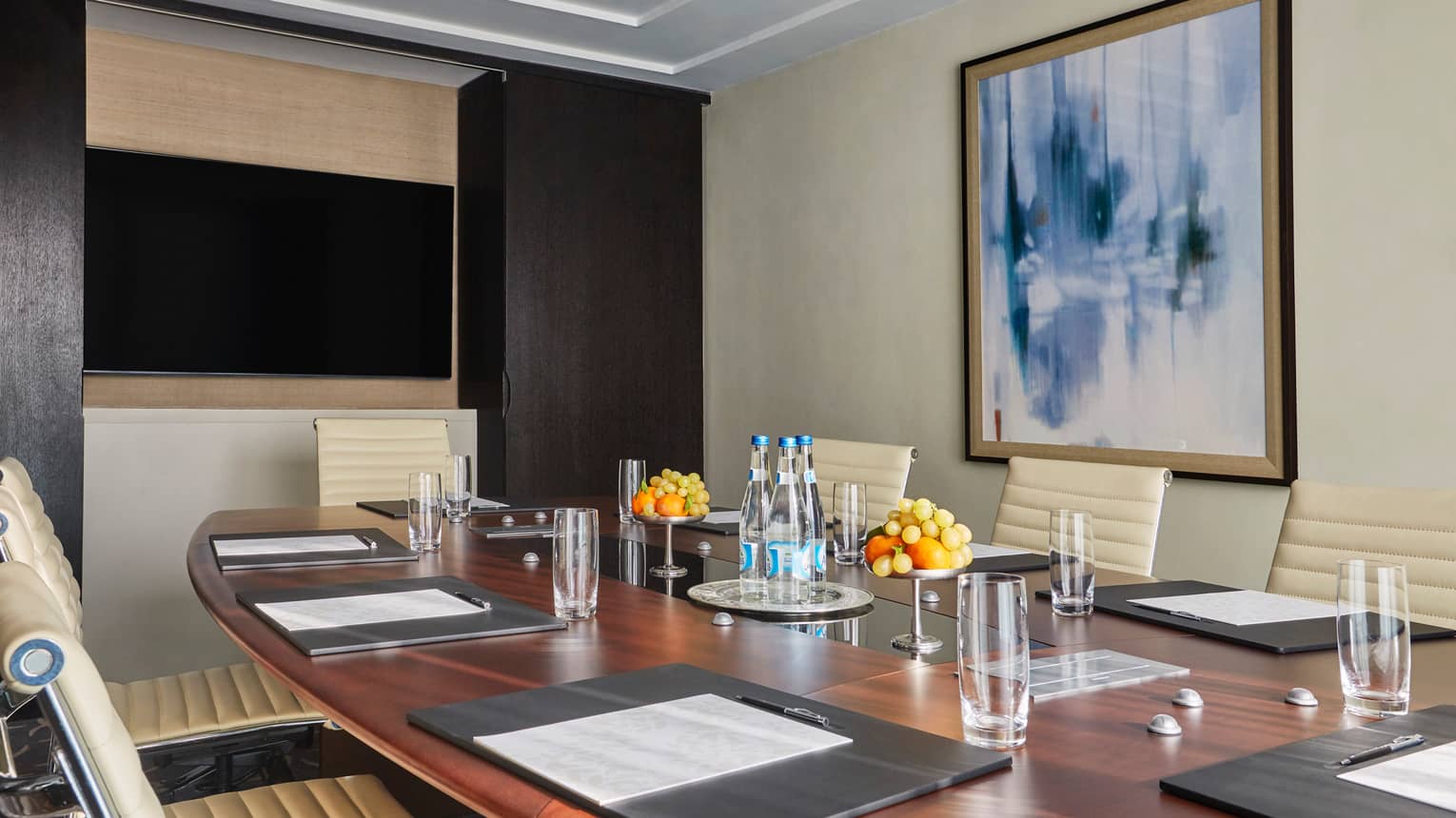 Large wood meeting room table with glasses, bottles of water, fresh fruit