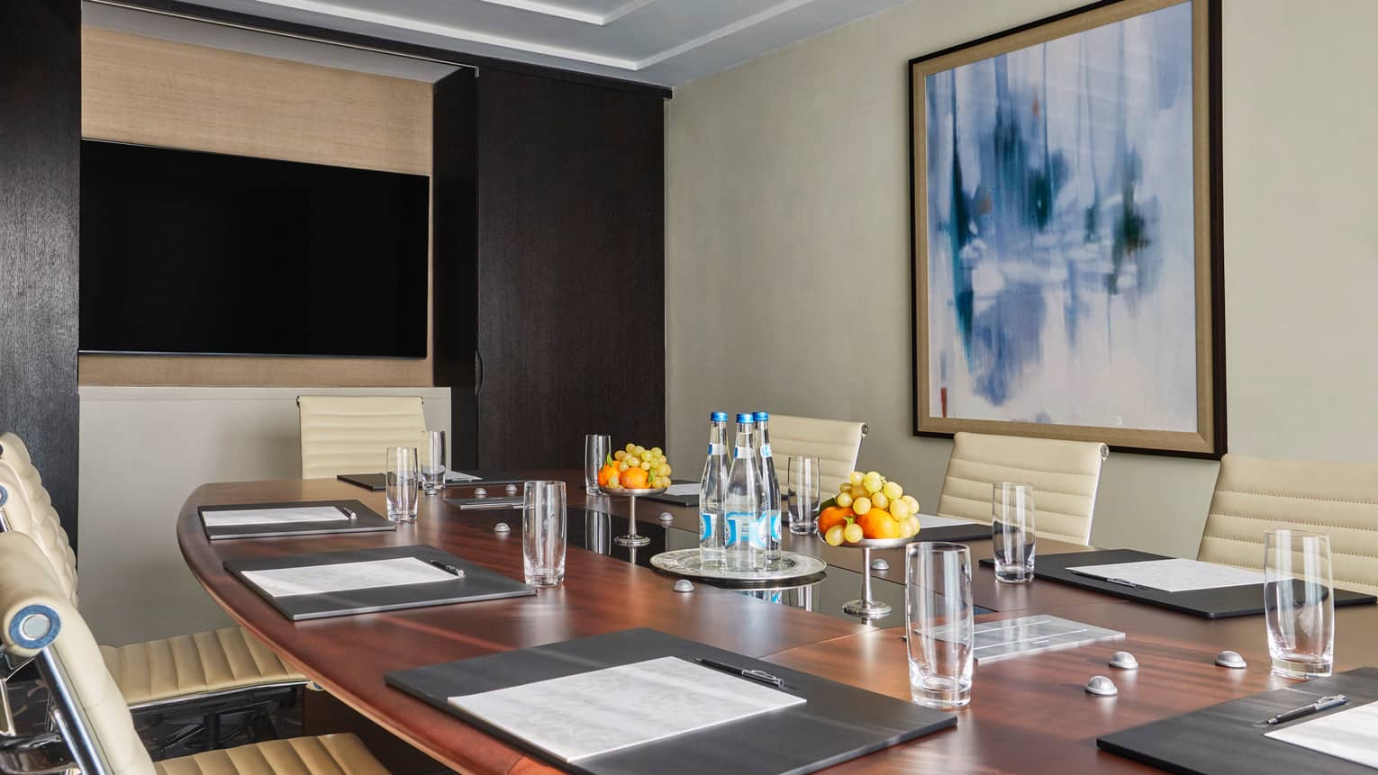 Large wood meeting room table with glasses, bottles of water, fresh fruit