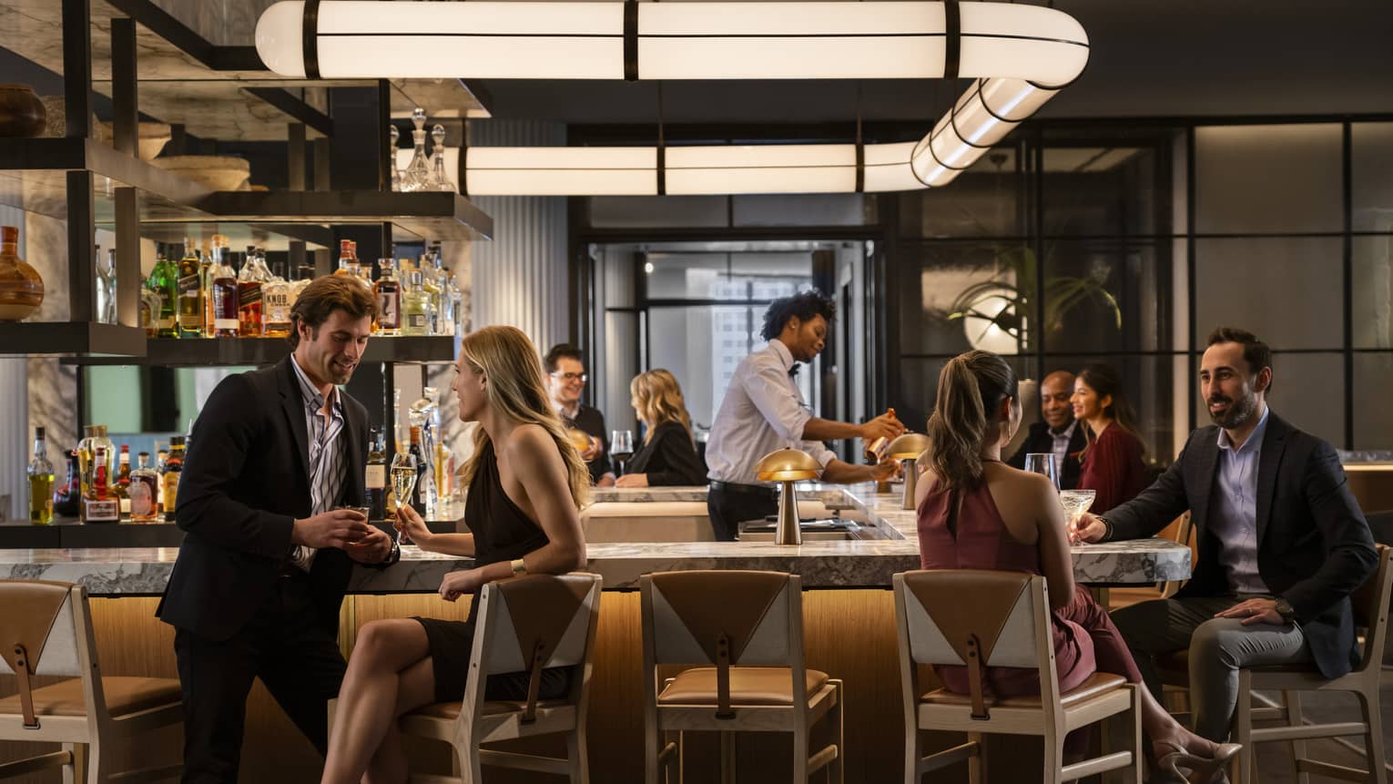 A bar area of a restaurant that is dimly lit with scattered groups of people sitting around it.