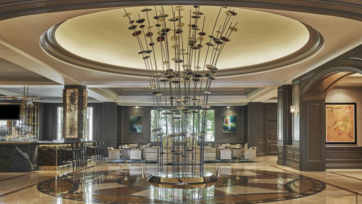 A tall sculpture with long metal extensions sits at the center of a marble lobby 