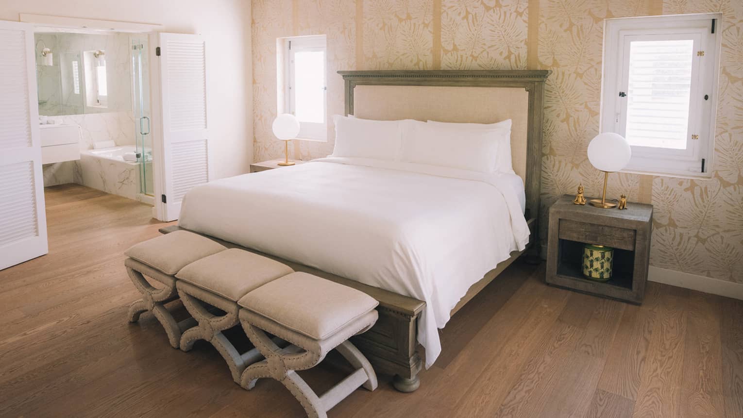 Bedroom with king bed, three stools at the foot of the bed, wooden floors and white wood vaulted ceiling