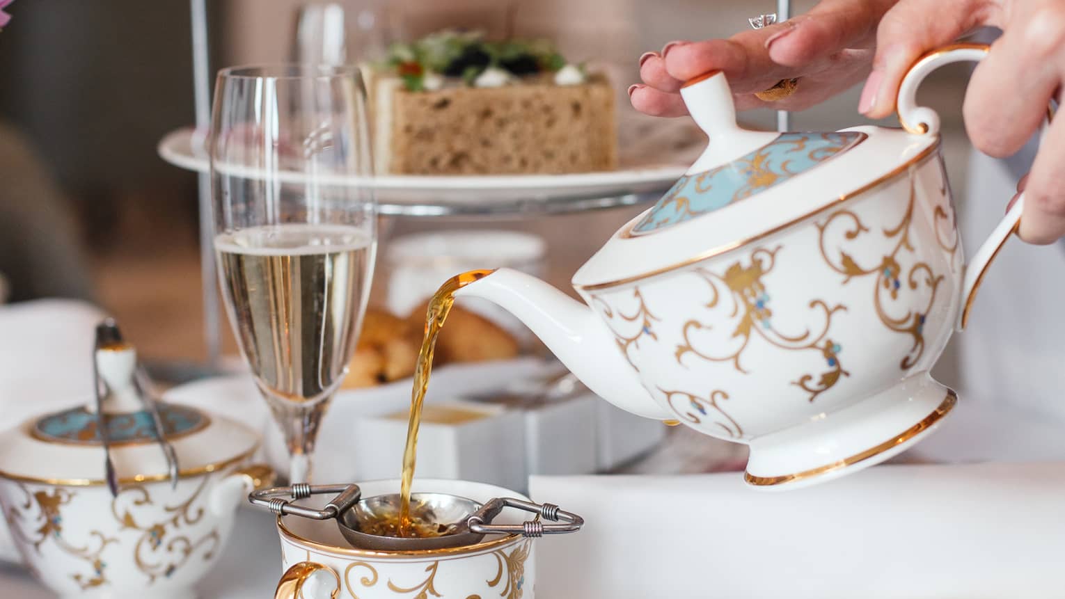 Hotel staff pours gold and white teapot by dessert tray at afternoon tea 