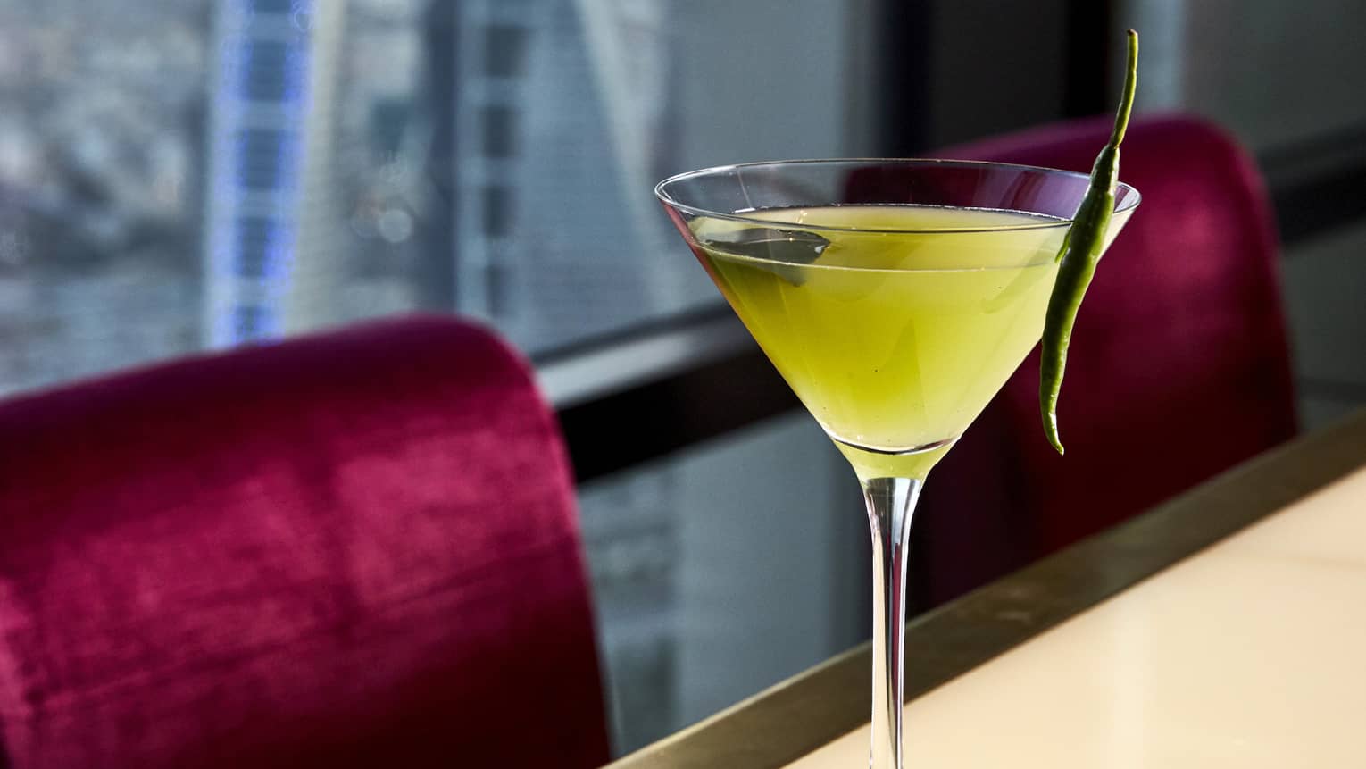 A yellow martini with a sprig of mint balanced on the lip of the glass. 