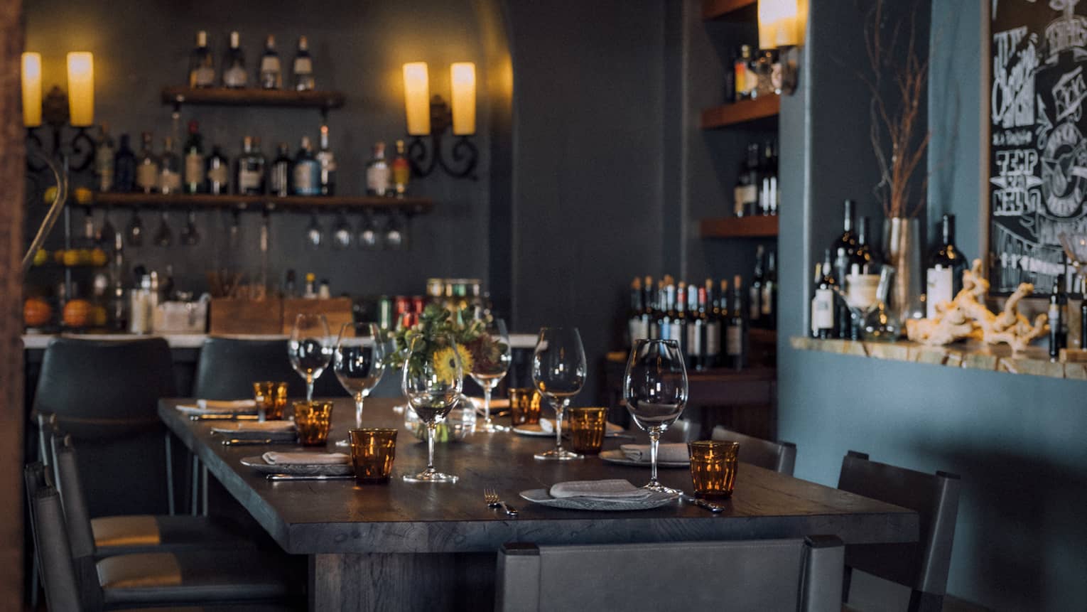 Dining room with candle light chandeliers and shelves of wine bottles.