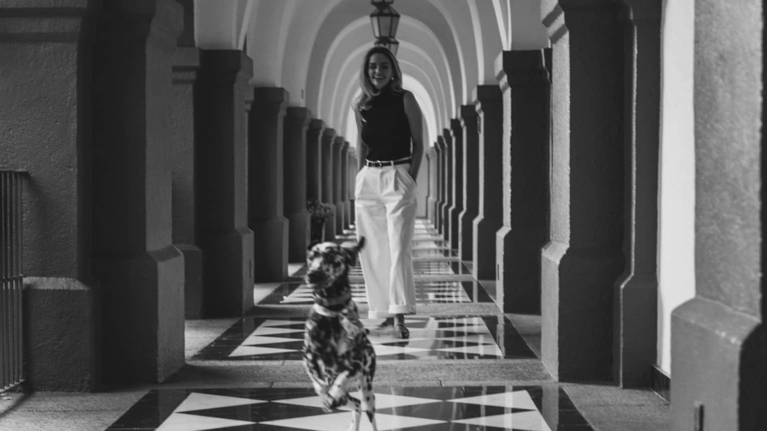 A person and a dog in an arched hallway with tiled floor and lantern-shaped lights hanging from the ceiling