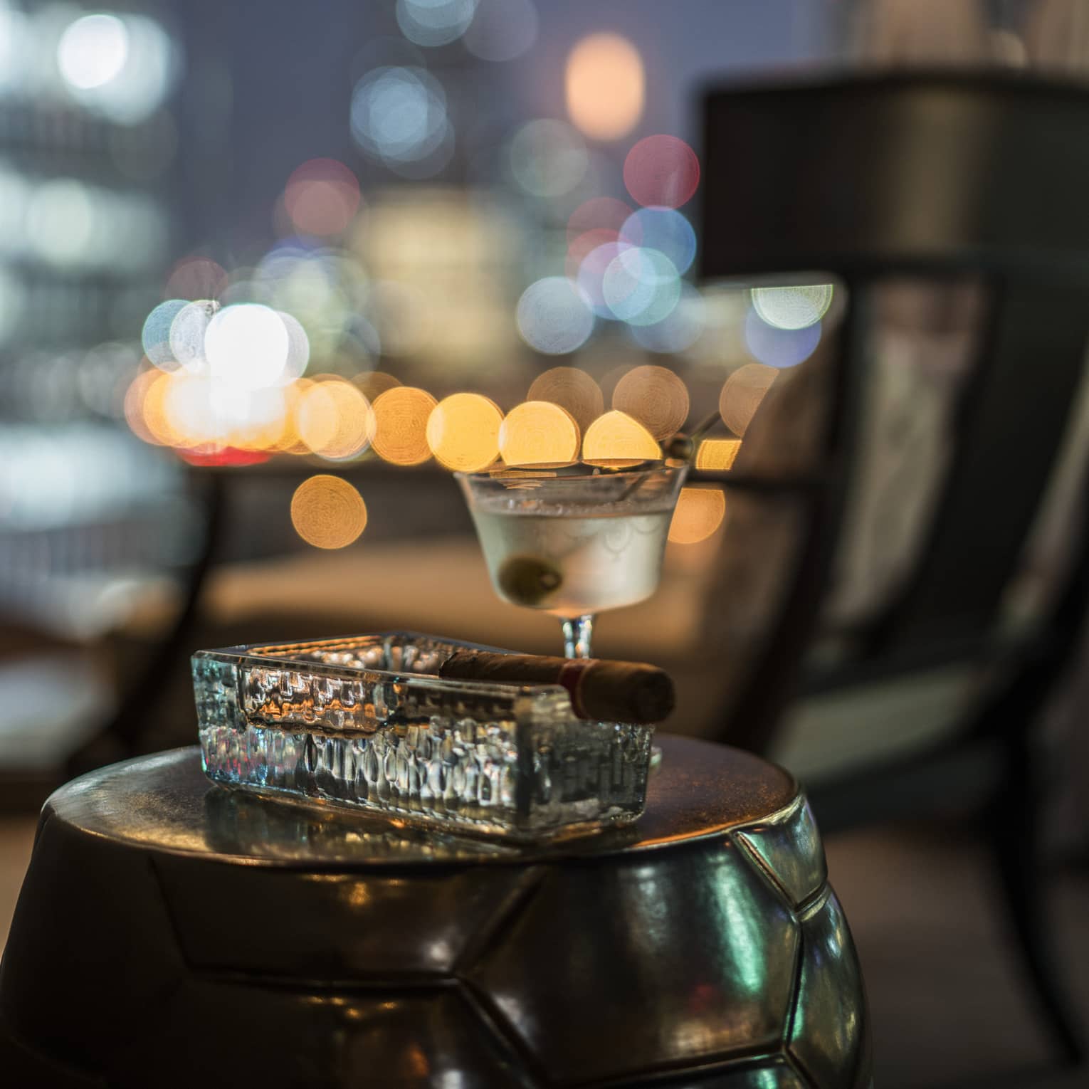 Cigar in heavy rectangular glass ashtray beside martini glass with olive 