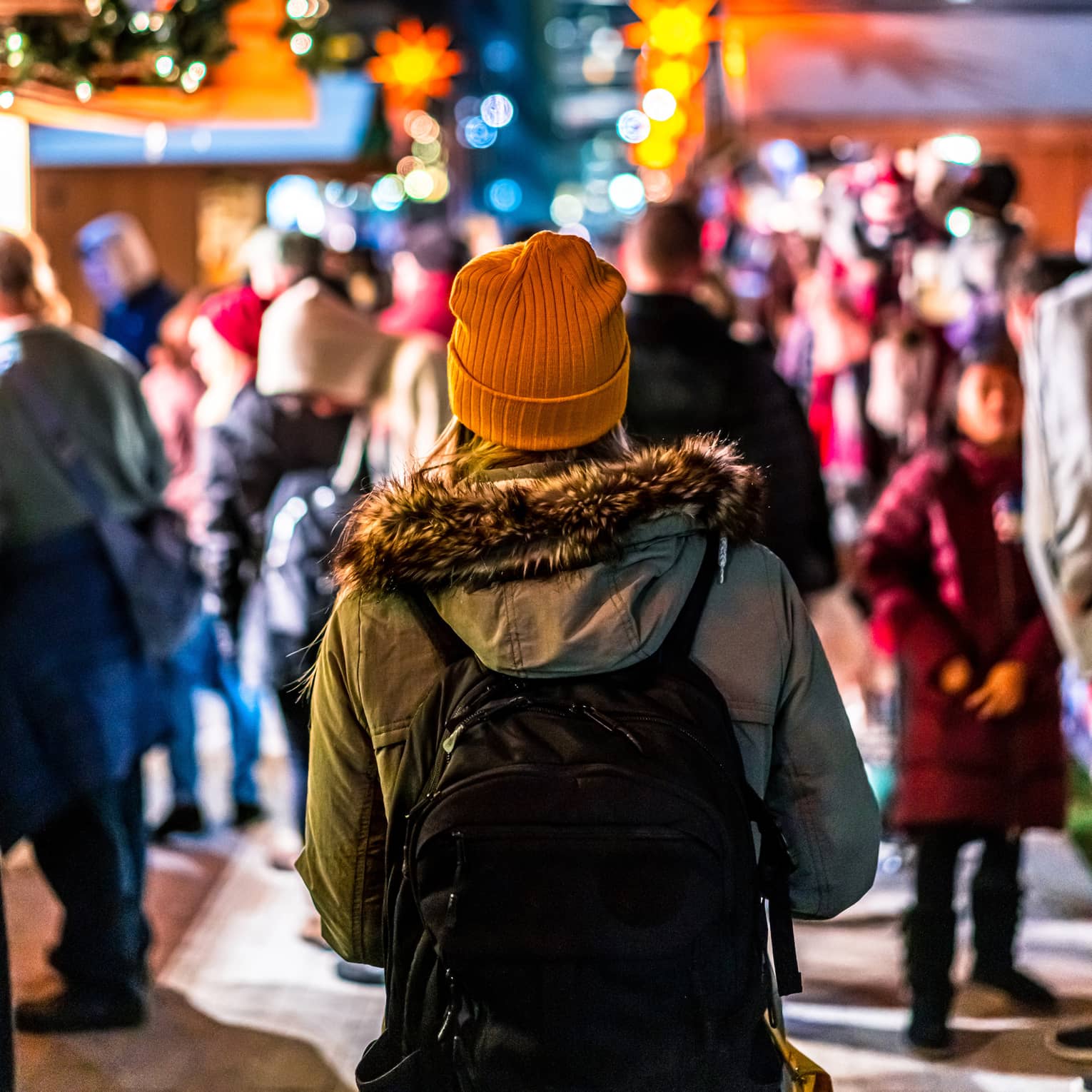 A young woman in an orange building walking in a crowd surrounded by Christmas decorations.