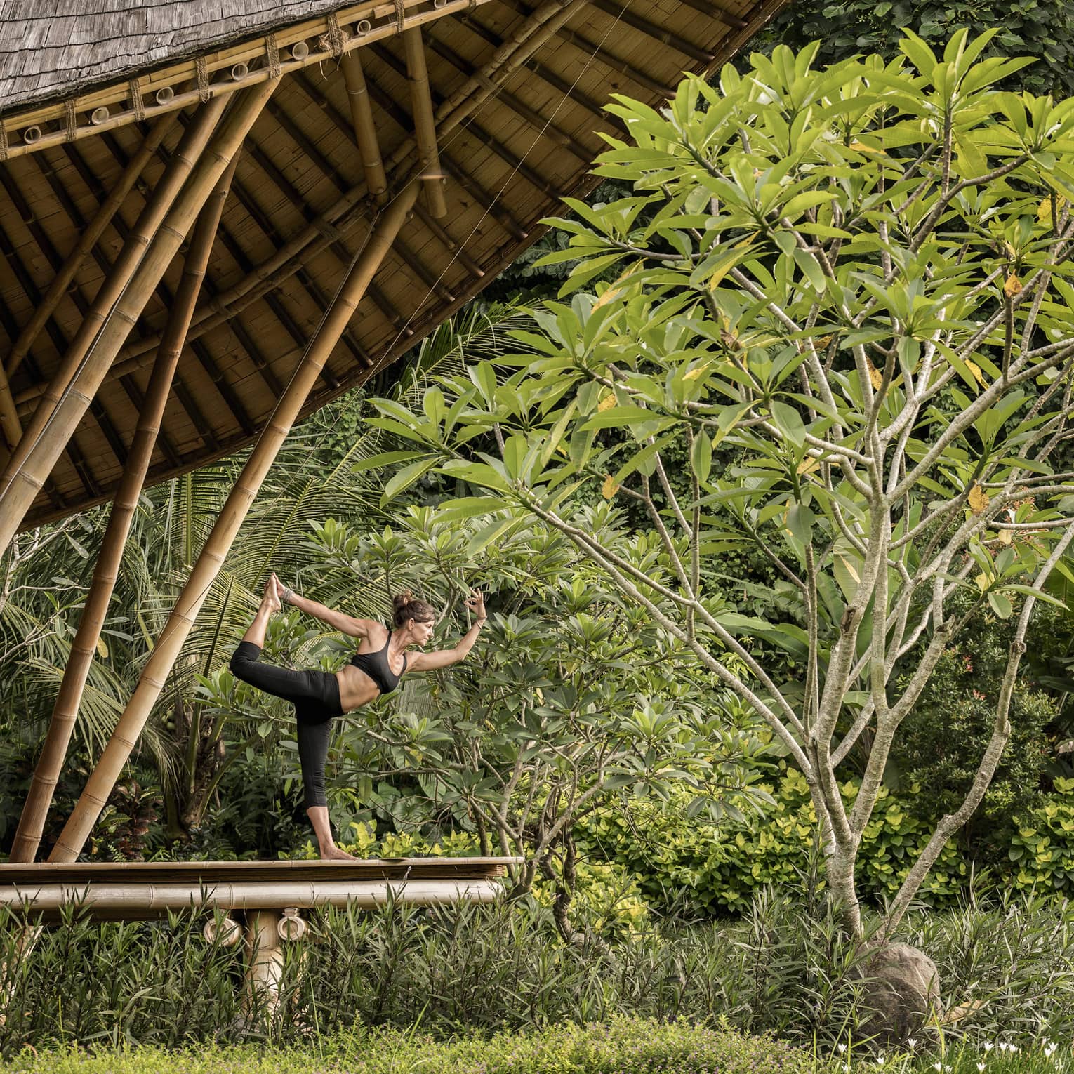 A guest with her arms and leg outstretched, doing yoga in an outdoor pavilion