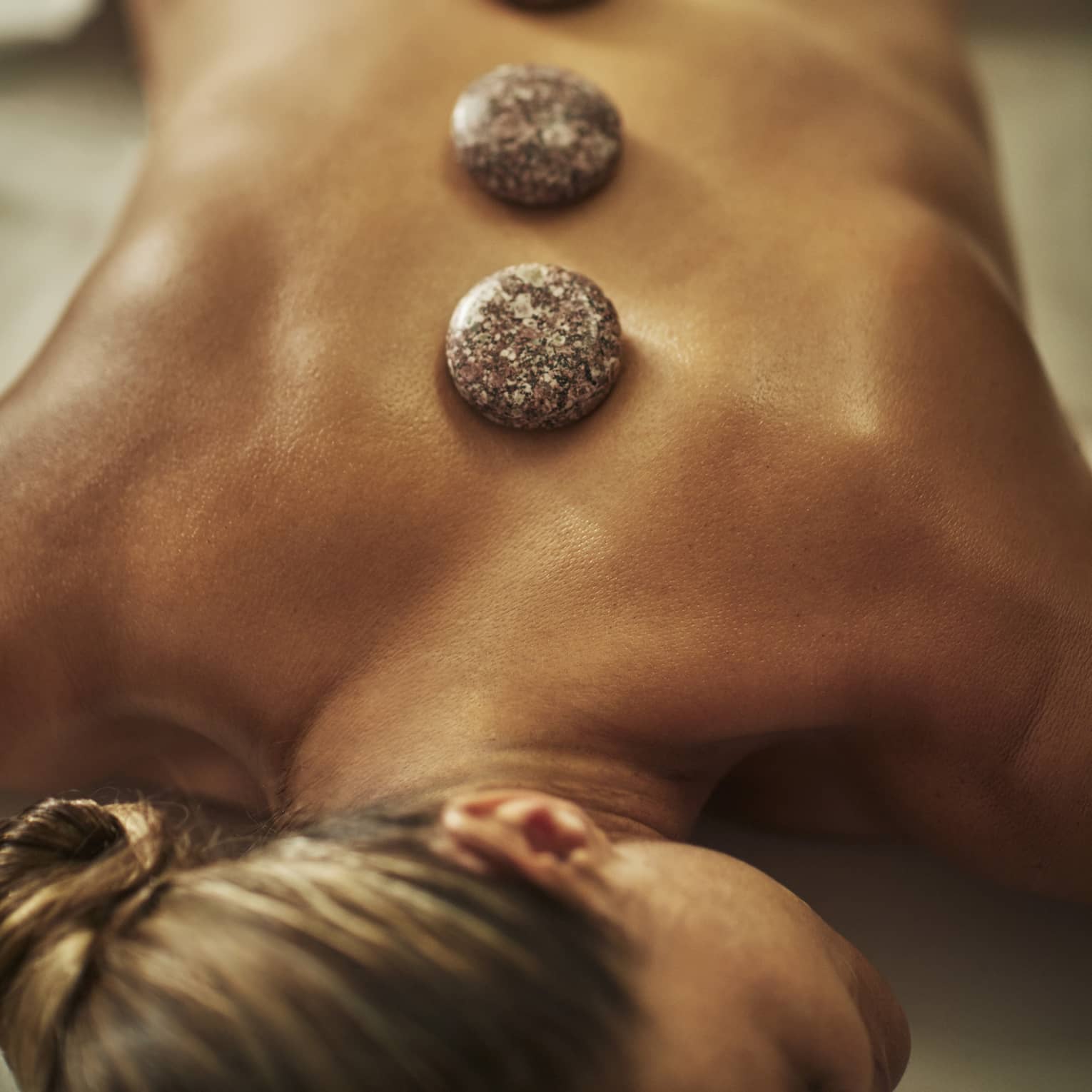 A woman lies on a spa table with four hot stones laid on her back
