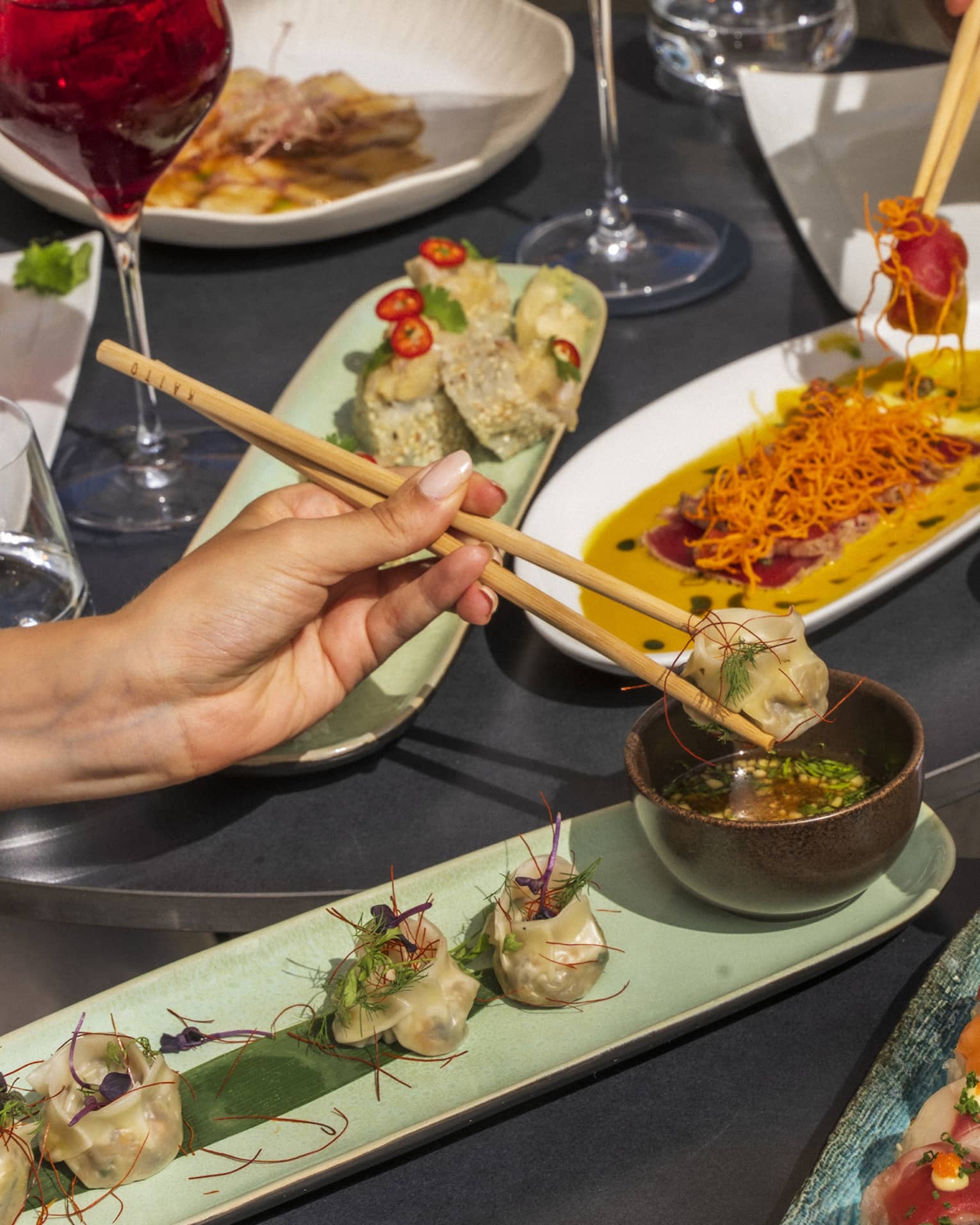 Three hands picking up sushi with chopsticks over plates of dishes
