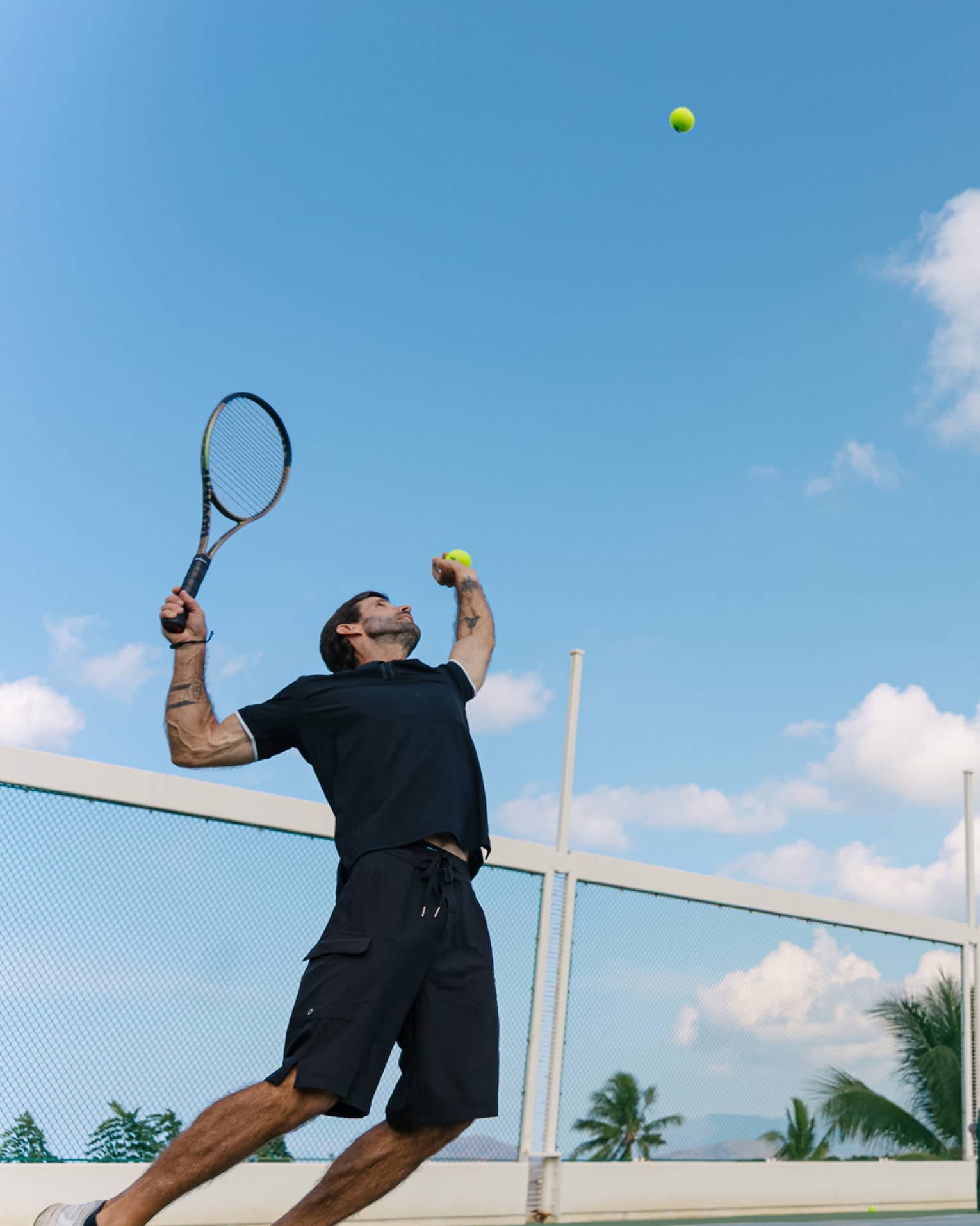 A man throws a tennis ball in the air, getting ready to serve