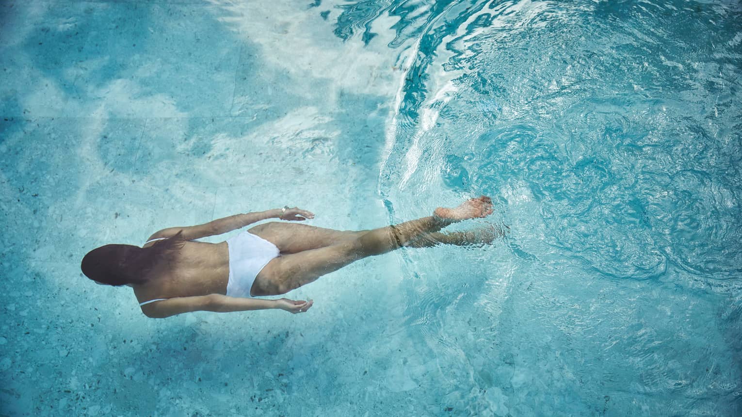 Woman in white swimsuit swimming underwater in blue pool