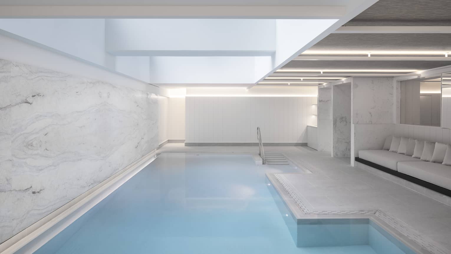 Indoor pool at spa, banquet of seating on one side, marbled wall on other 