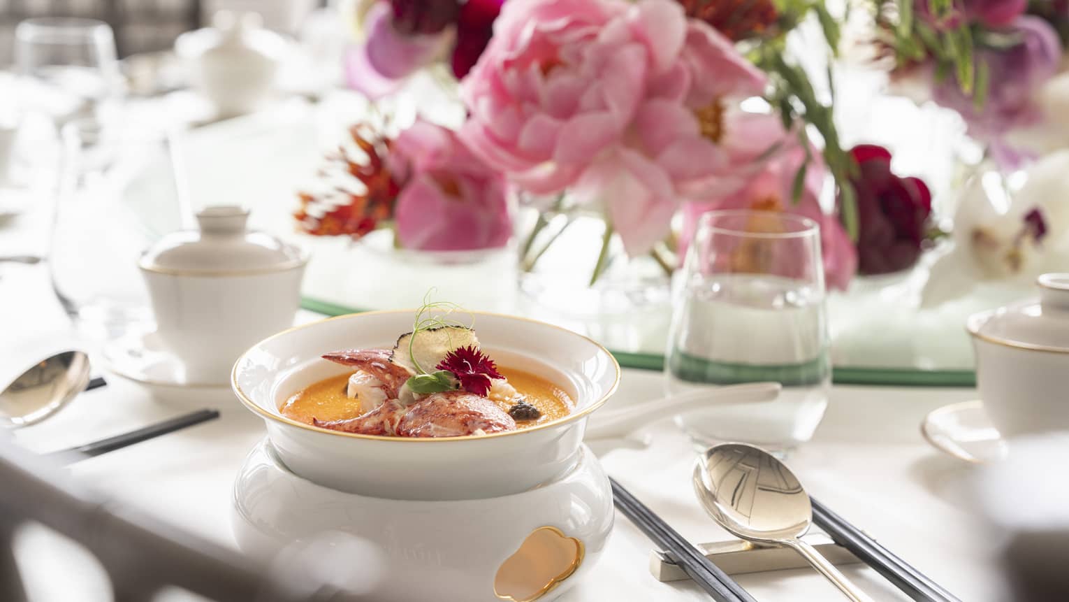 Table setting with white bowl of soup, pink floral centrepiece