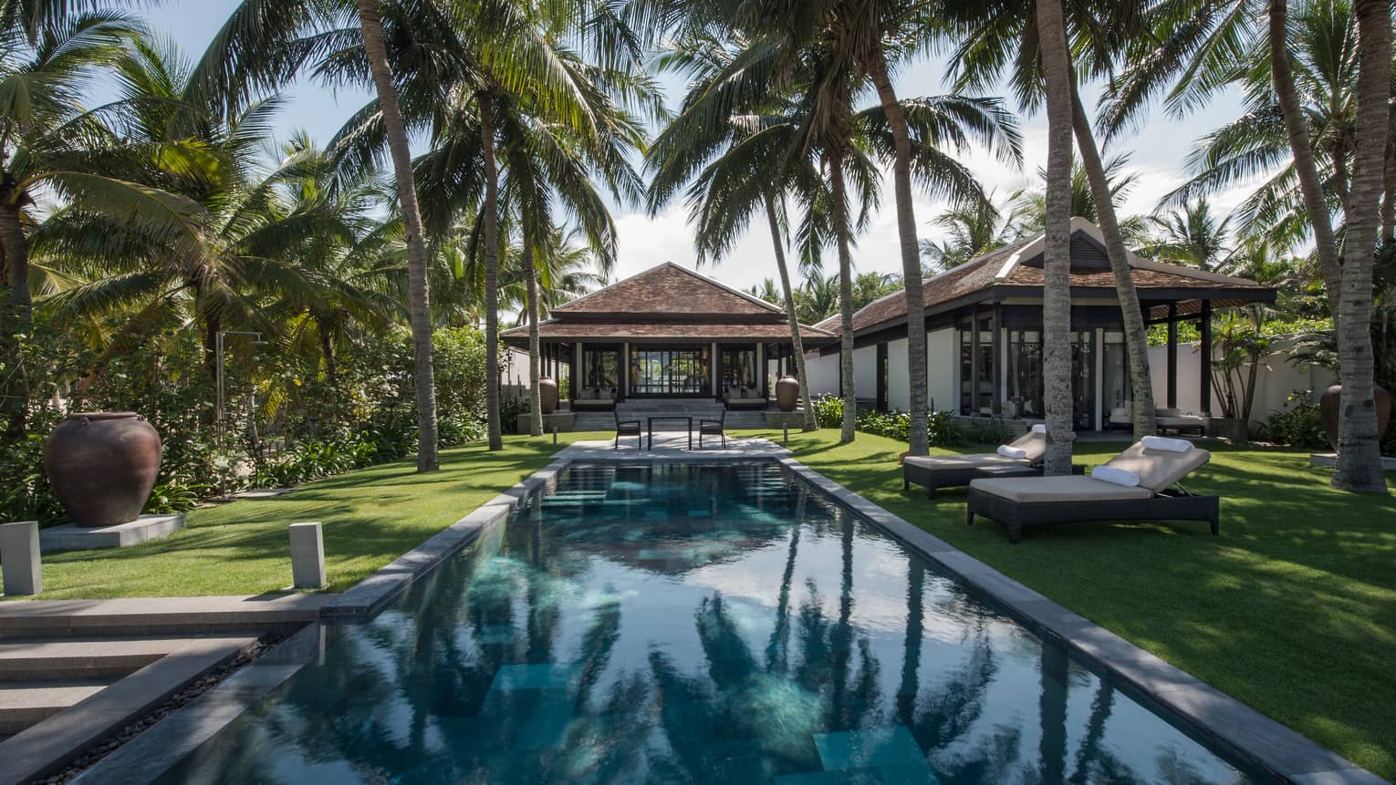 Pool villa, small patio table at end of outdoor swimming pool under palms