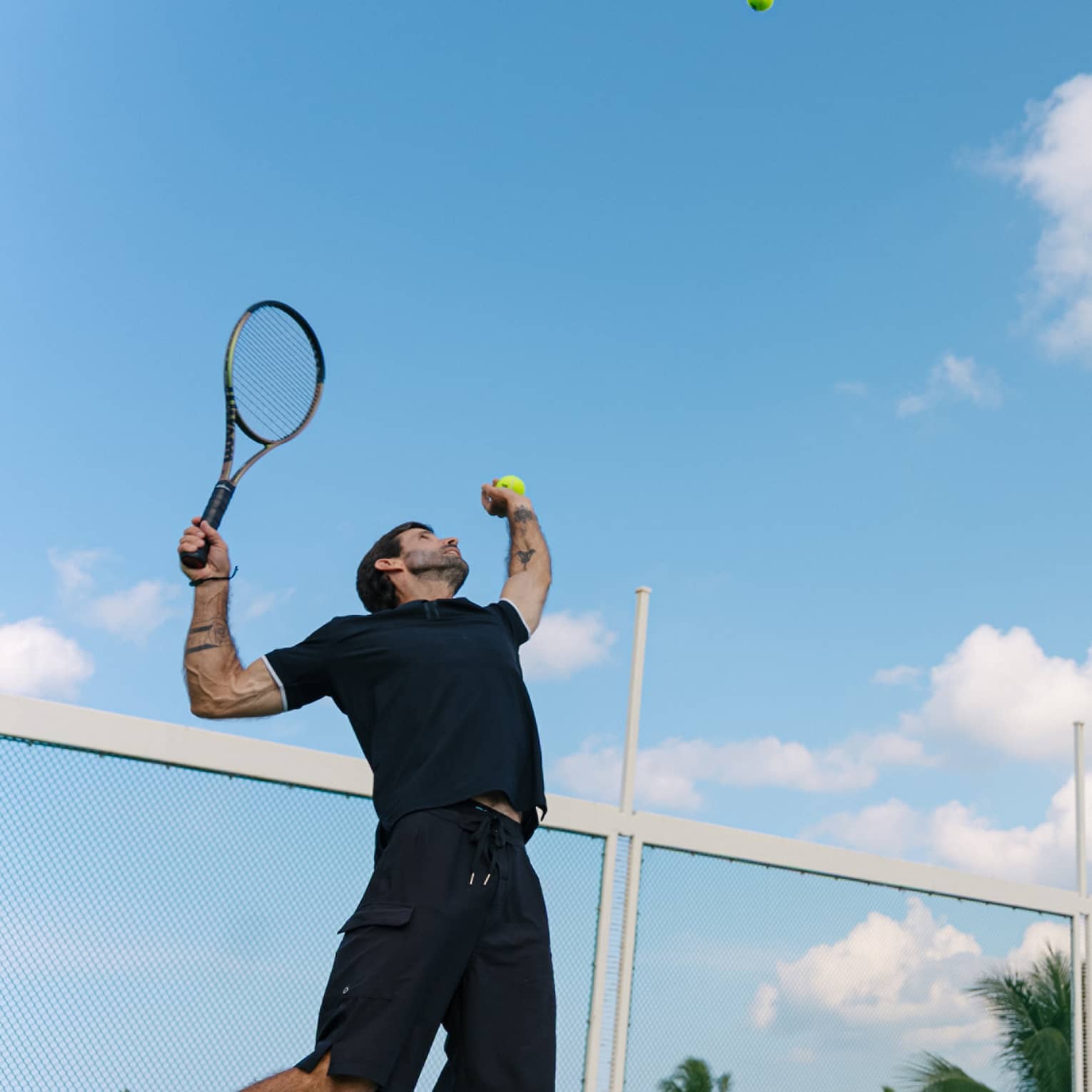 A man throws a tennis ball in the air, getting ready to serve