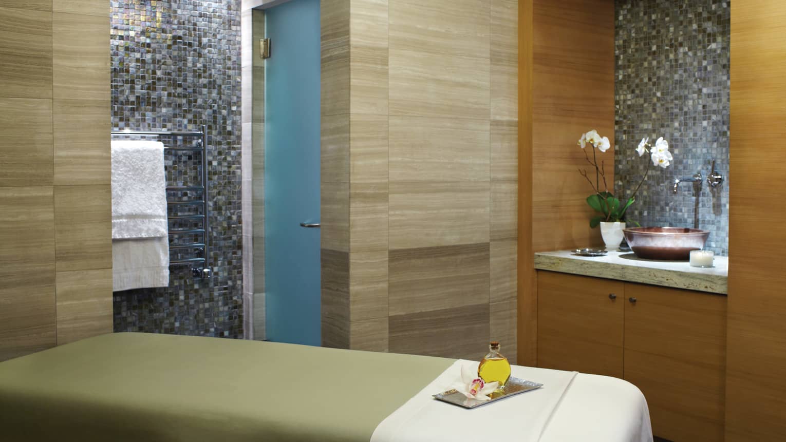 Massage table with green blanket, white sheet, wood and tile walls, sink