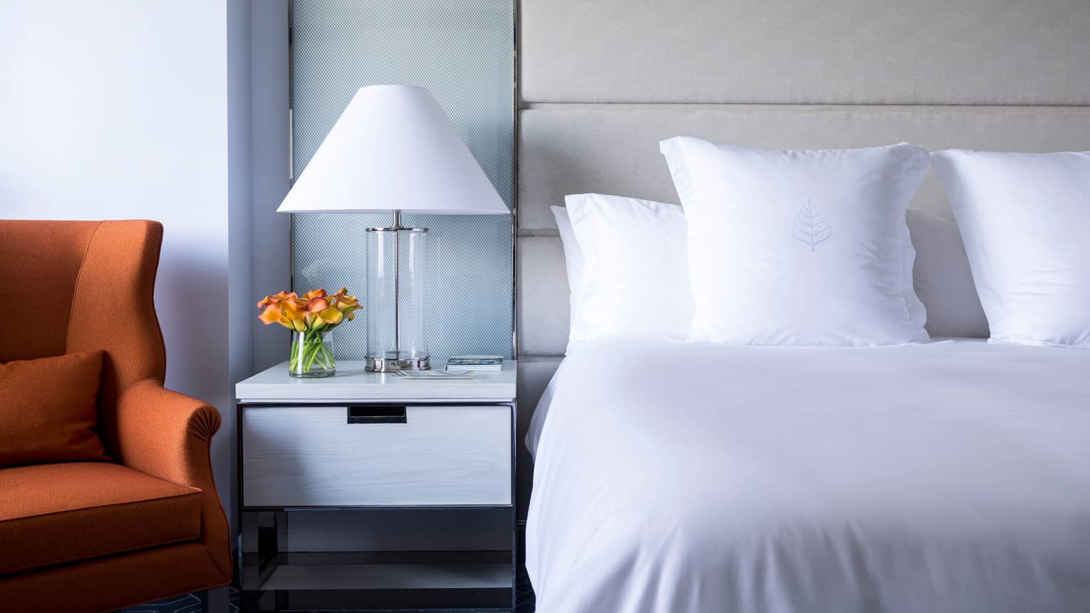 Midtown Deluxe Room close-up of crisp, white bed and linens, lamp next to orange accent chair