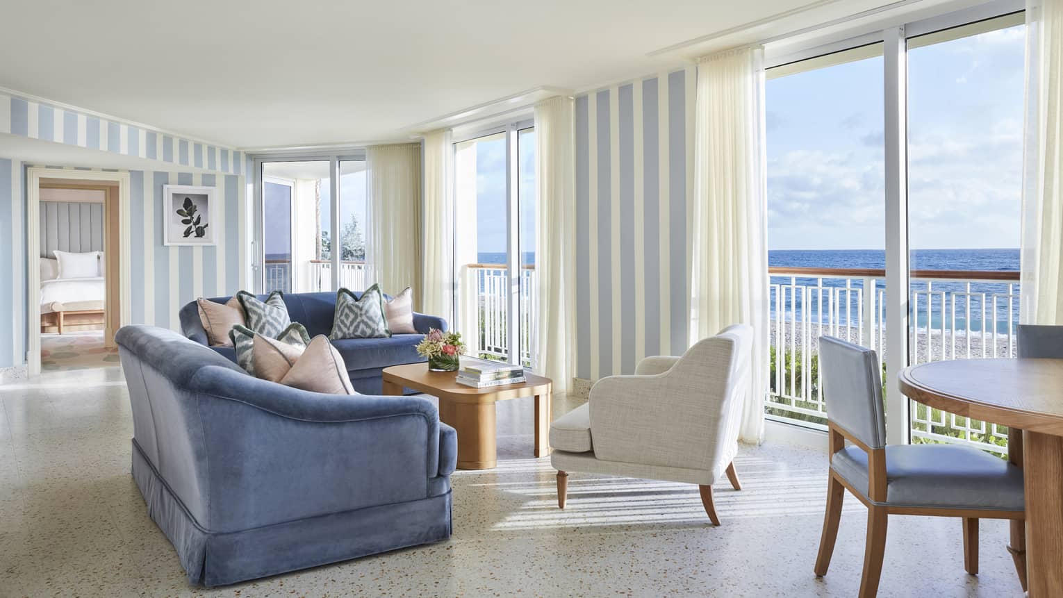 Living area in a suite, with blue sofas, a white armchair and floor-to-ceiling views of the ocean