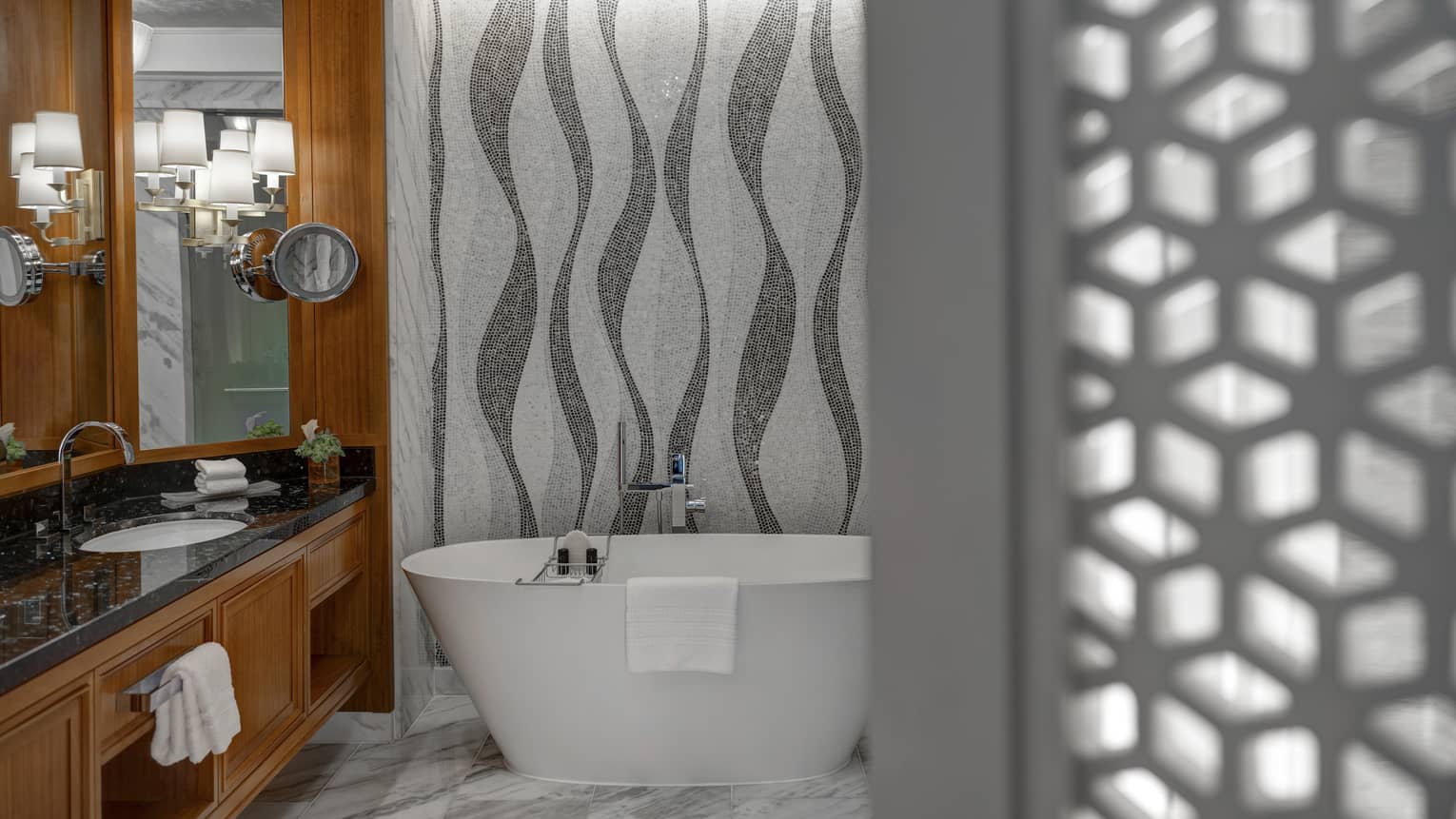 Bathroom with mosaic tiled walls, freestanding tub, vanity with black top