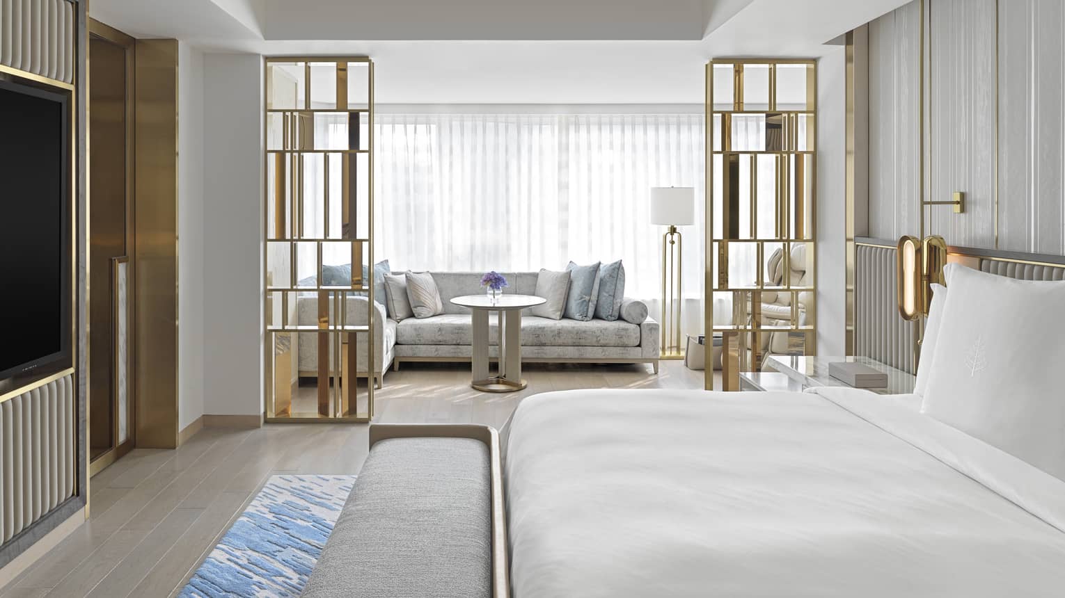 Dynasty Suite with King bed, gold accents and decor, white sofa with light blue pillows, natural lighting
