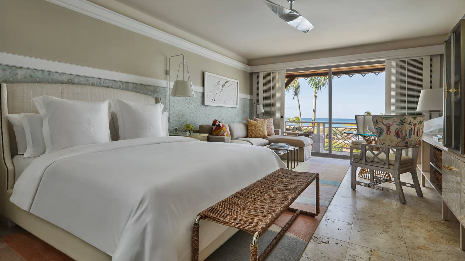 Light shines onto a large bed and marble tiled floors from the outdoor patio