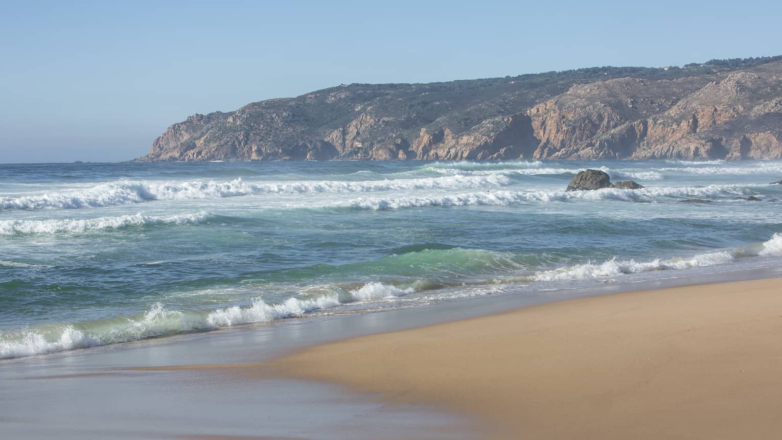 Blue waves roll onto shore on serene Guincho Beach in Portugal 