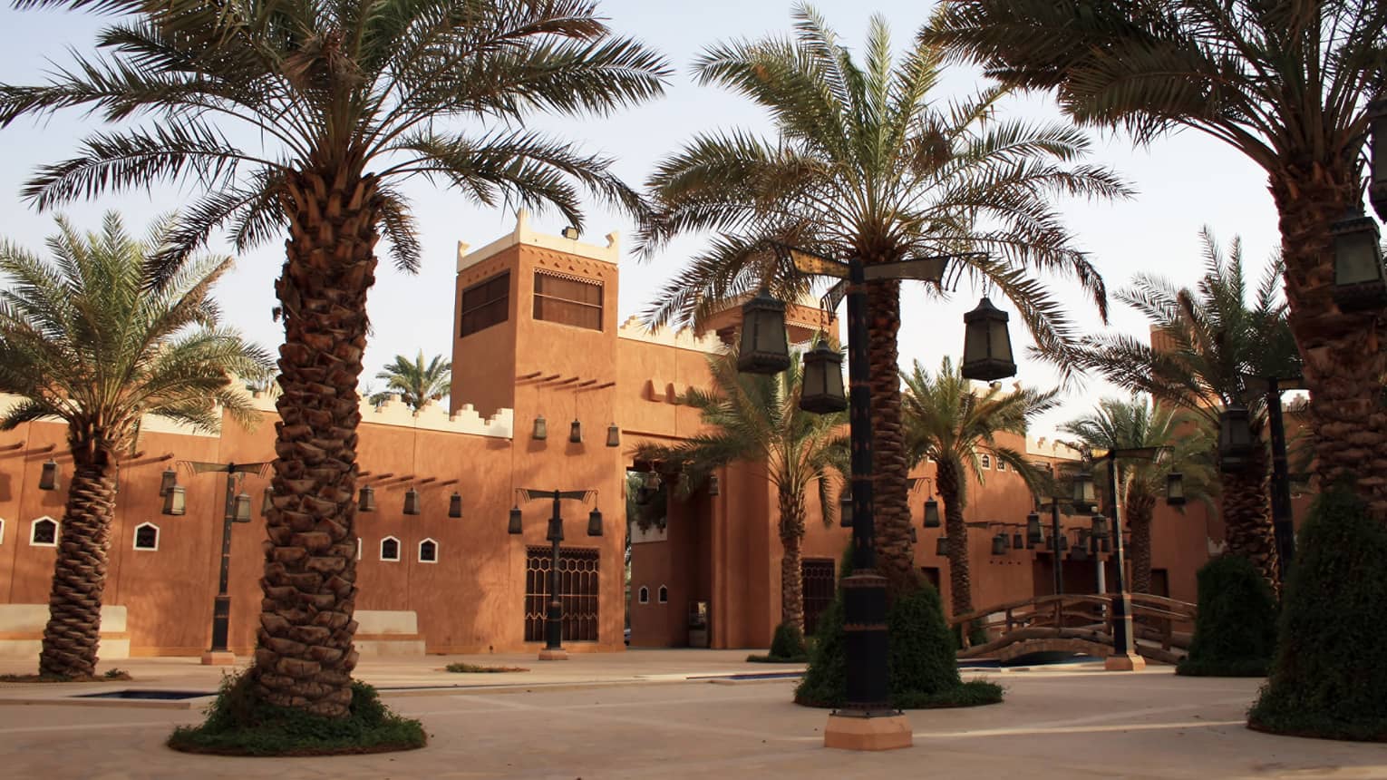 Sunny exterior of sandstone building and large palm trees with lanterns hanging from branches