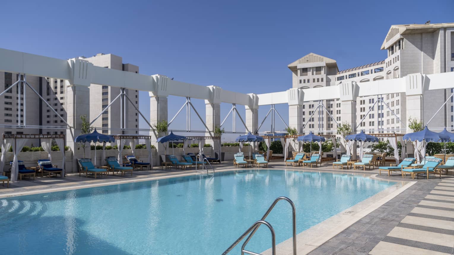 Outdoor pool surrounded by teal lounge chairs and white column