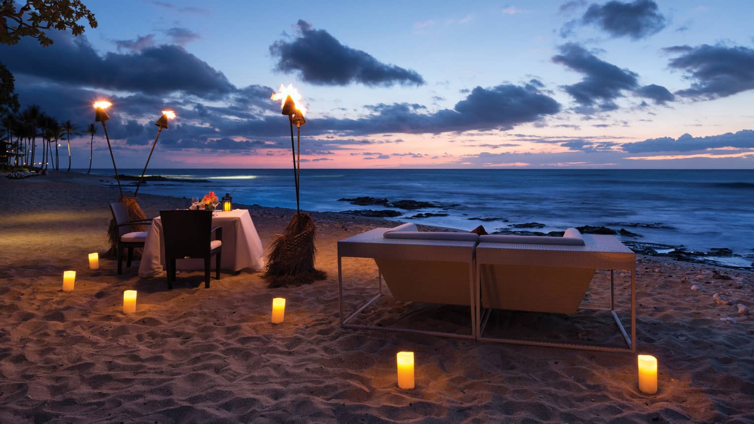 Torches over dining table on beach at night, glowing candles in the sand