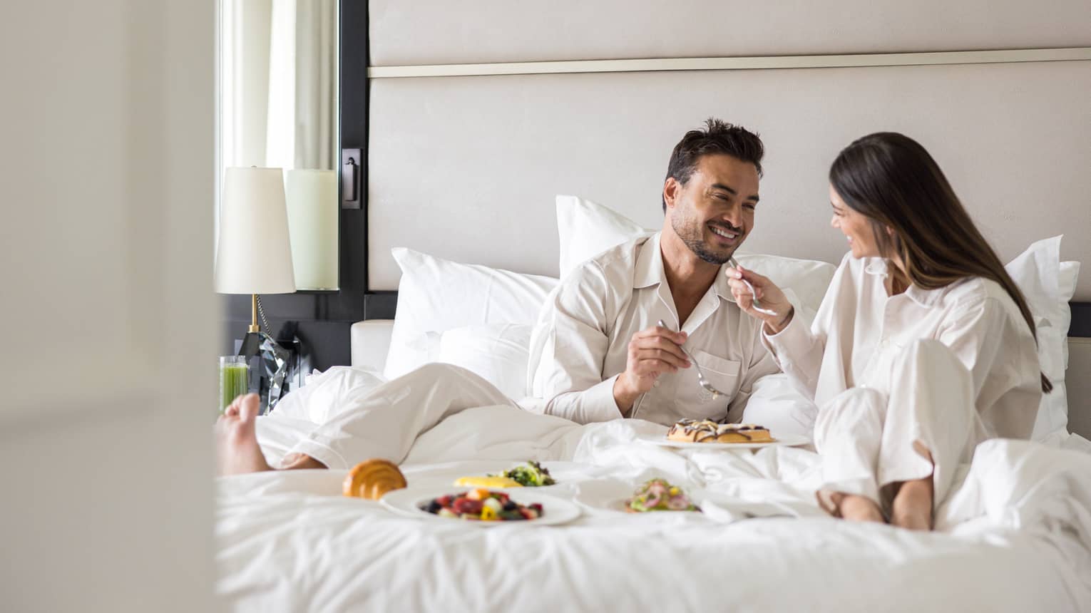 Man and woman eat breakfast in bed in luxury hotel room