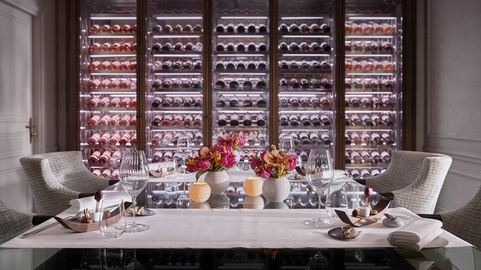 A private dining room with two chairs and an illuminated wall of wine on display