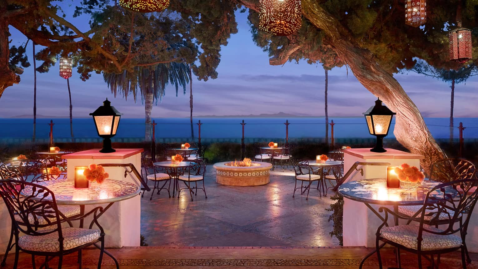 Bella Vista patio at dusk with candle-lit tables under lanterns on posts, hanging from trees
