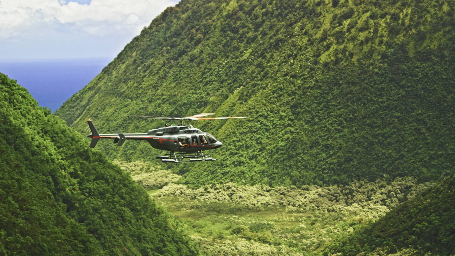 Orange and grey helicopter flying through crevice between green mountains