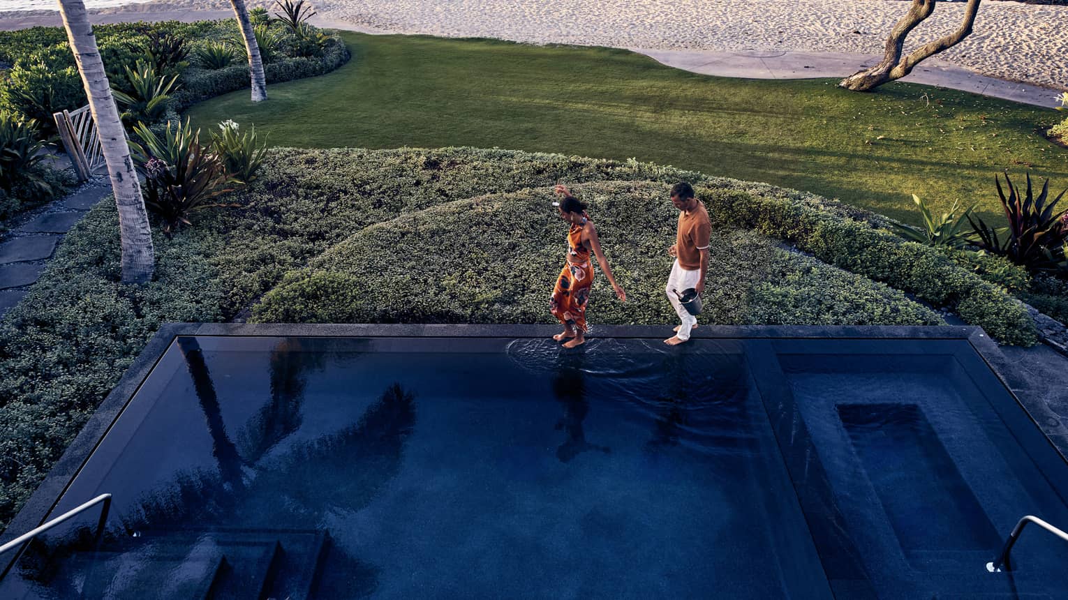 Two people walk along the edge of an infinity-edge pool