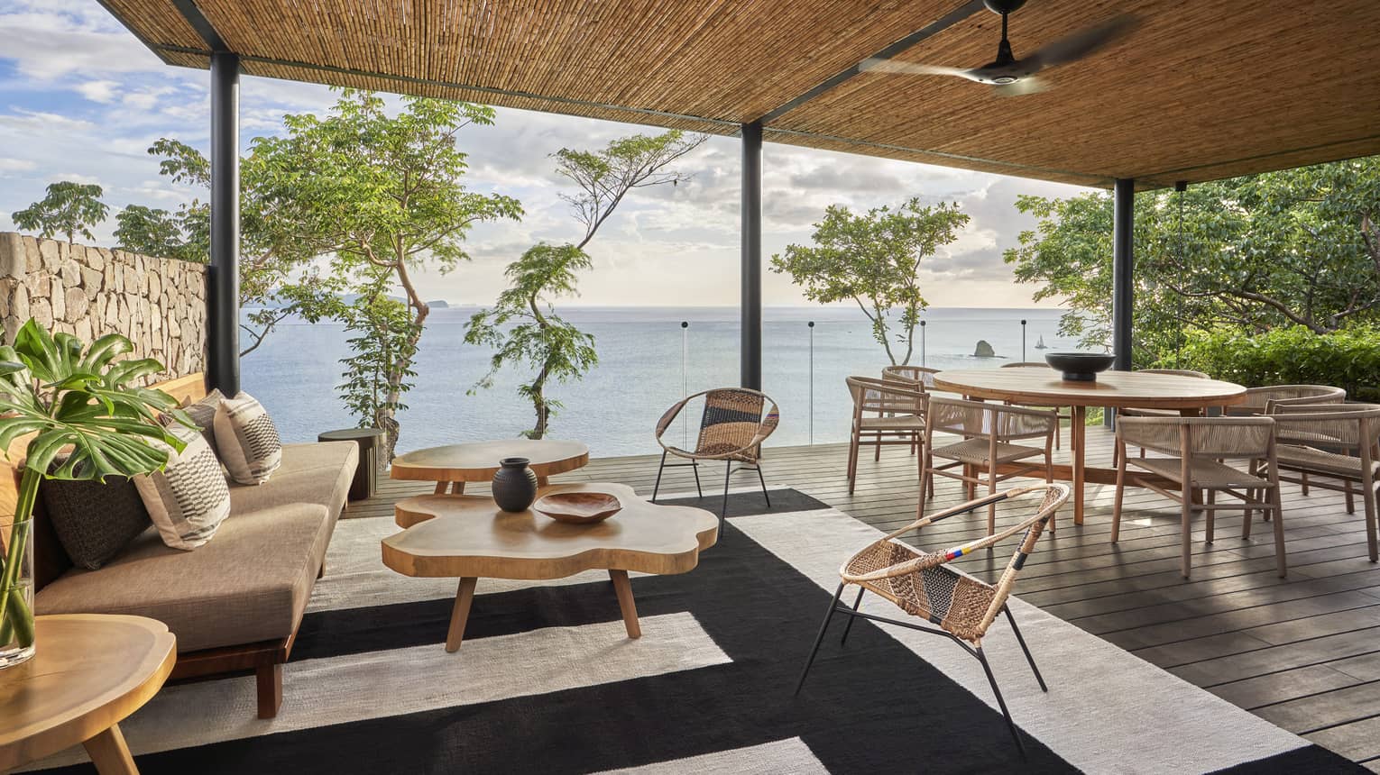 Covered outdoor wooden deck with dining table and contemporary lounge furniture overlooking the sea