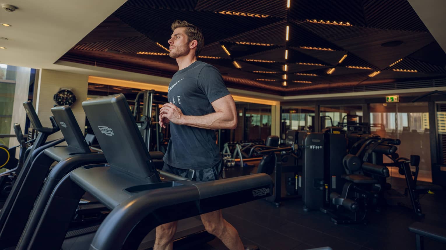 Man wearing dark grey t-shirt and shorts runs on a treadmill in a hotel gym