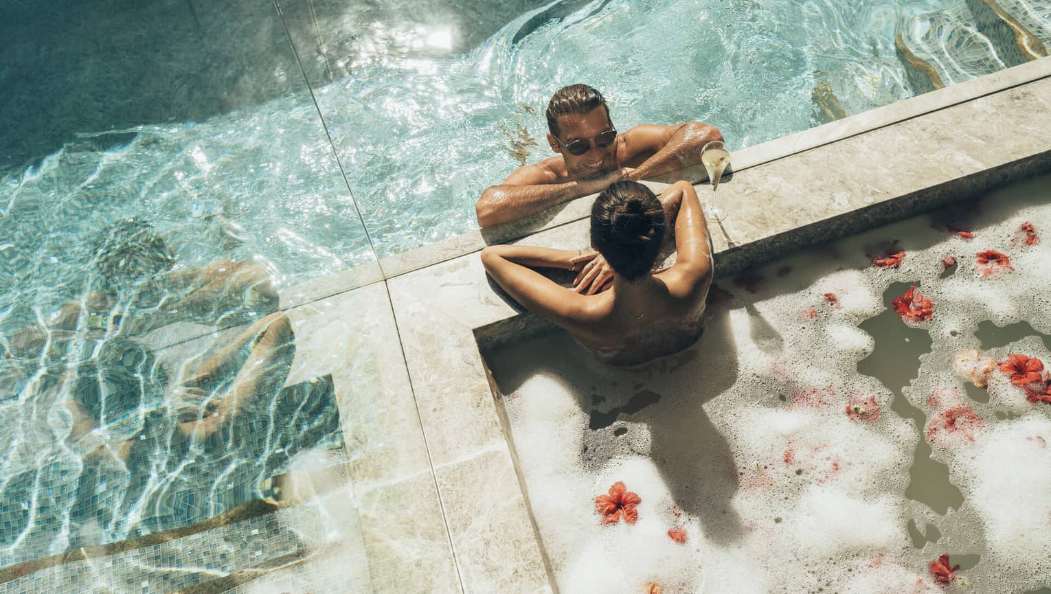 A couple enjoying an outdoor bath filled with bubbles and flower petals