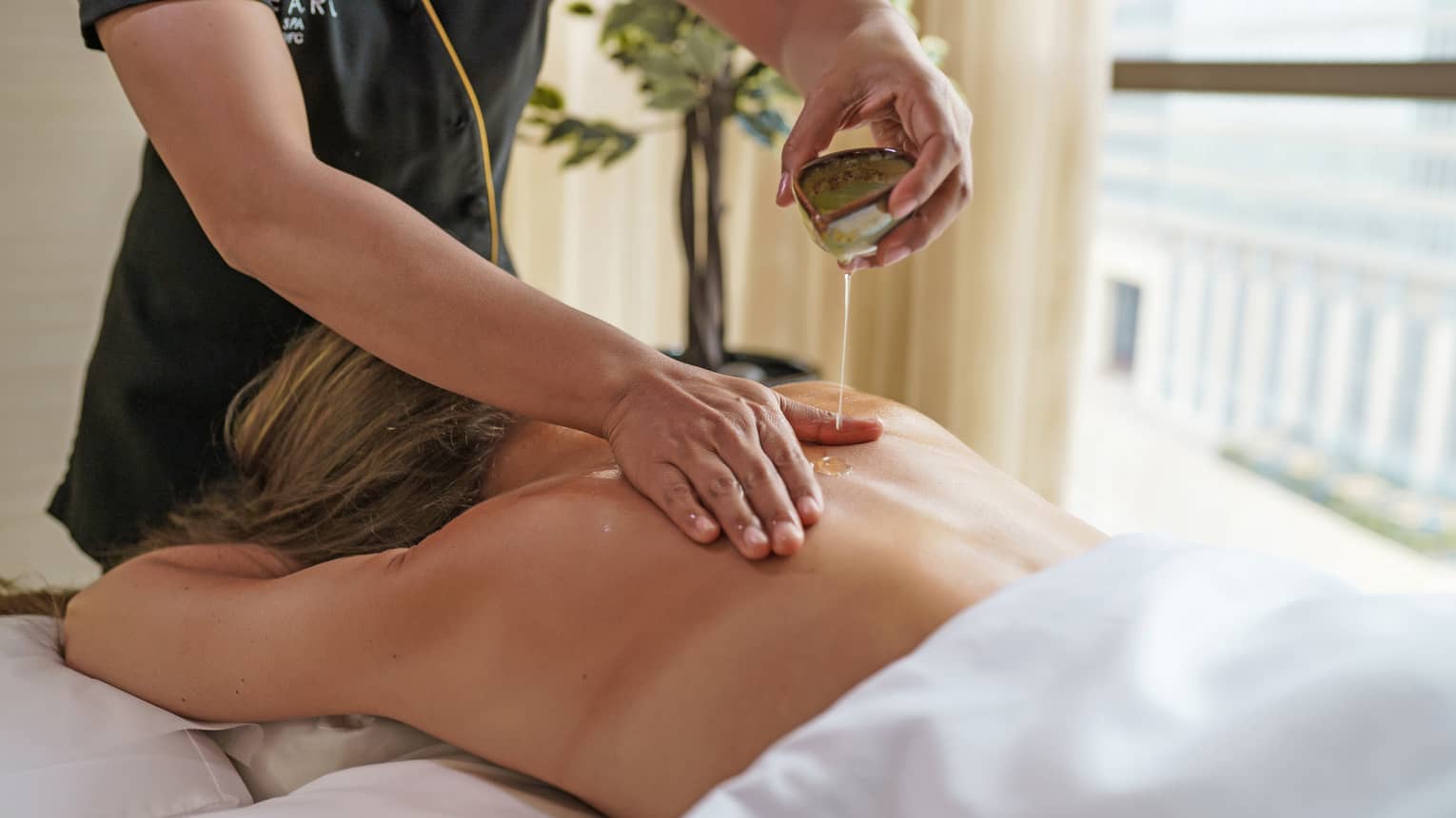 Guest lies face down an a massage table covered in a white cloth as a masseuse spreads oil on the guest's back
