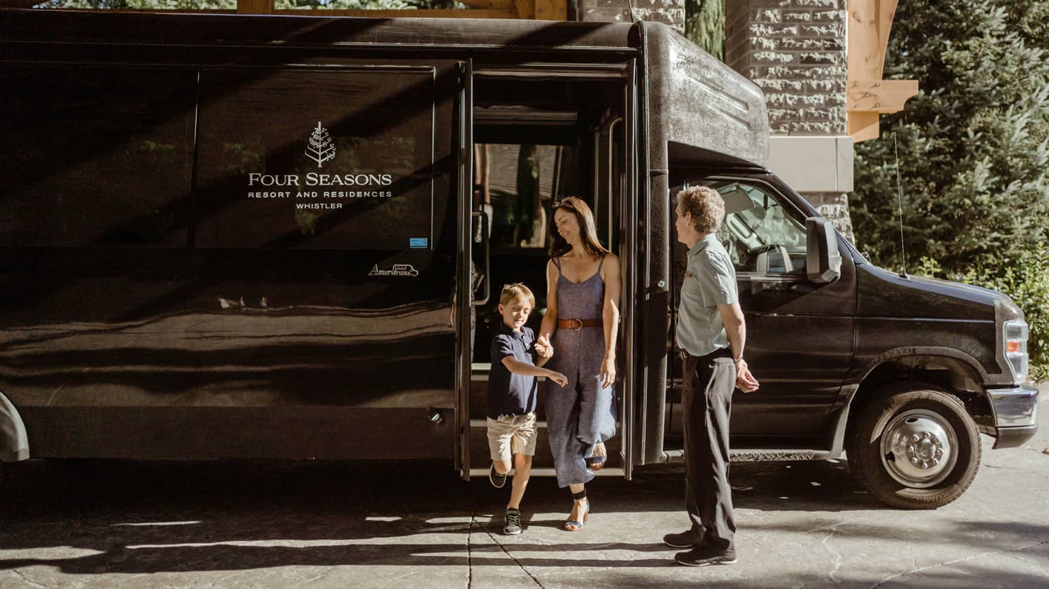 A family steps off of a black Four Seasons shuttle bus, underneath the shale stone entryway.