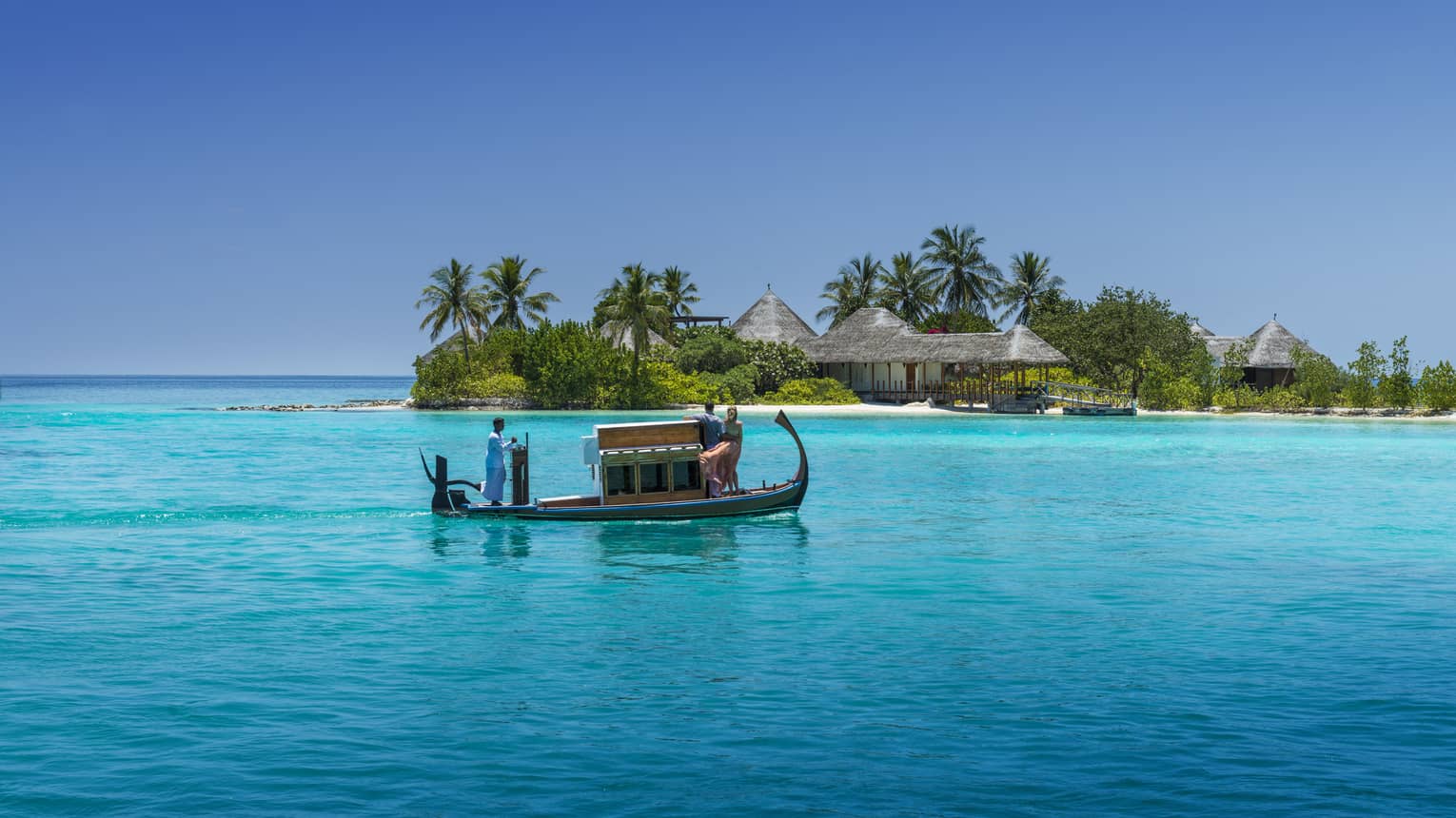 A wooden boat with passengers travels over clear turquoise water toward a tropical island spa with palm trees and thatched-roof villas