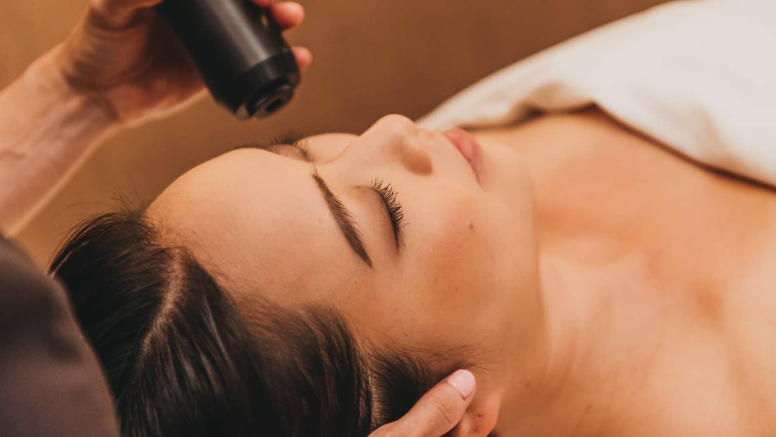 A spa staff member applies a cryotherapy treatment to a woman's forehead