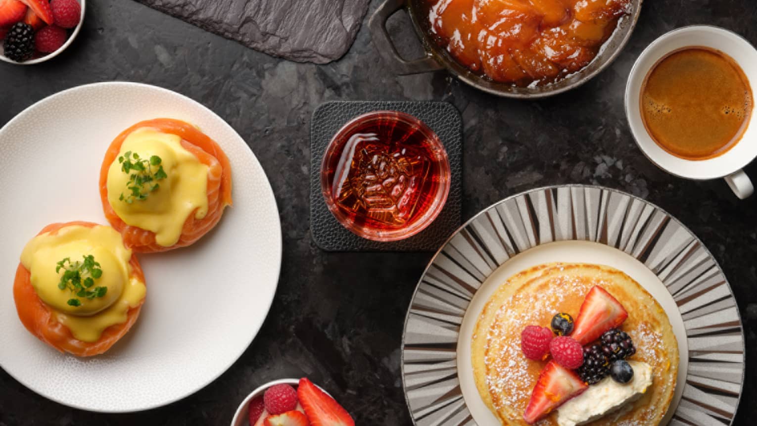 Brunch plates with pastries, fruits, pancakes and coffees on black table